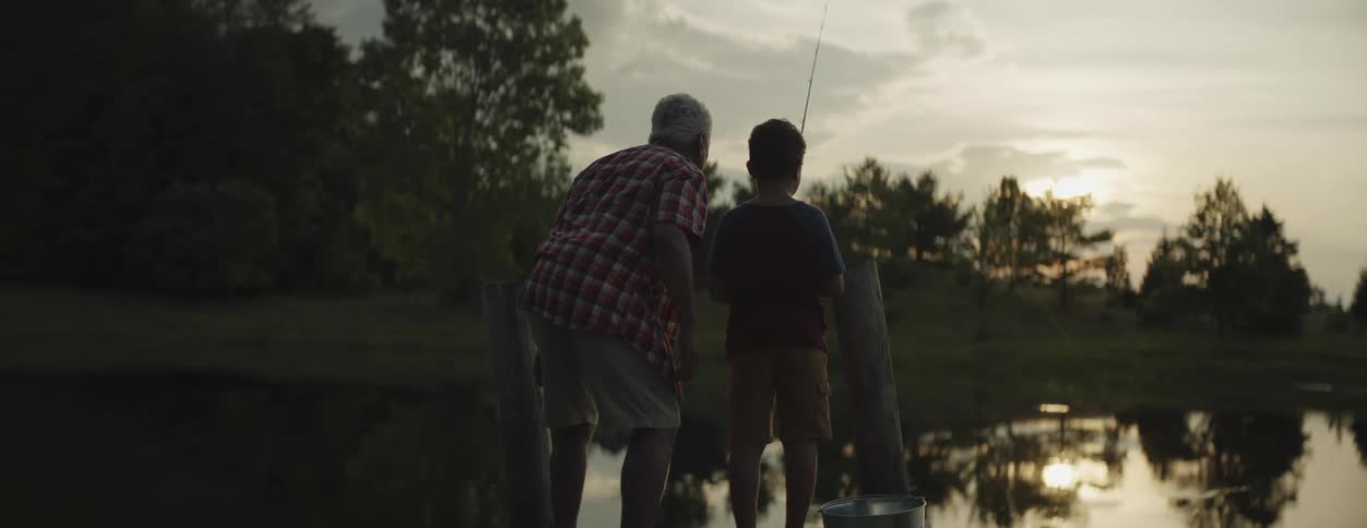 Son and father are fishing outside next to the lake