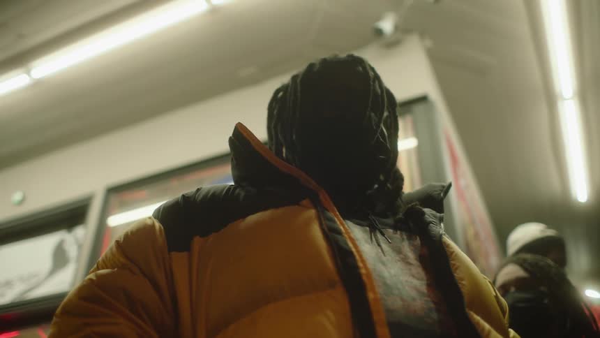 People wearing winter coats and masks stand waiting for a train