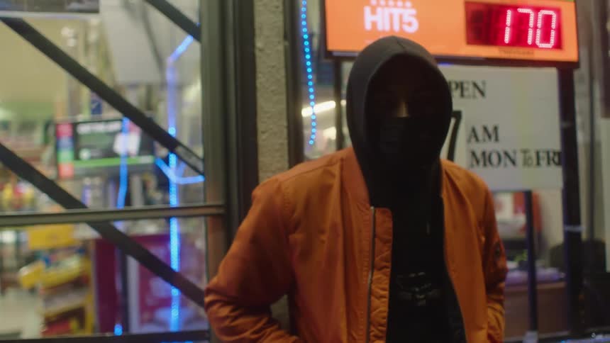 A young black man is standing outside at night next to a store