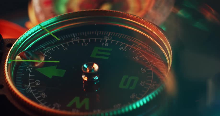 An open compass jiggles with movement as colorful light reflects on its glass surface