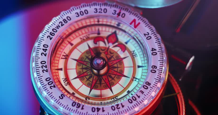 The needle on a compass spinning with colorful light glowing and a wind rose on the face