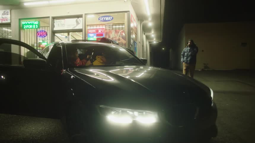 A group of people linger around a car outside a convenience store