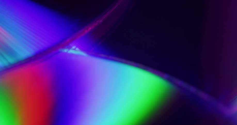 Neon lights flash off a pile of shiny compact discs