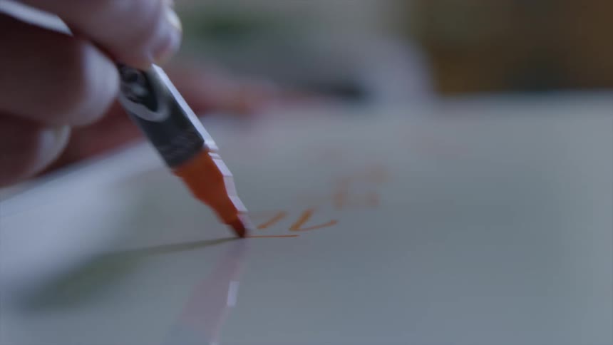 Person writes on white surface using orange marker