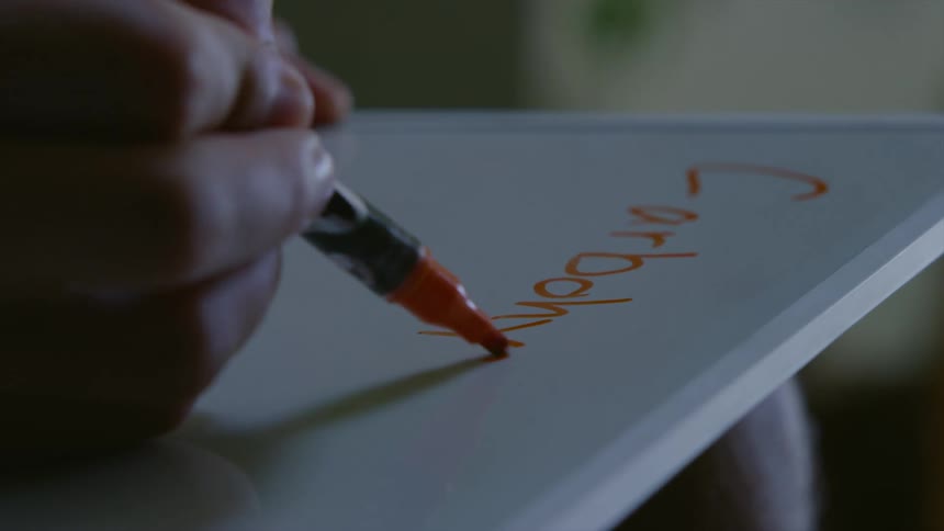 Person writing on a board on her lap with a red marker in a dimly light room