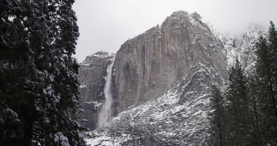 A waterfall is pouring off the top of a snow covered mountain