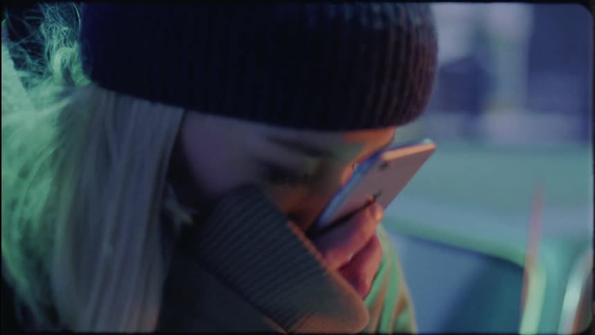Blonde woman with black wooly hat and green coat in cold weatheruses smartphone