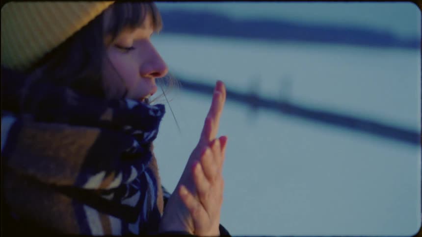 Woman blows on hands to keep them warm while outside in snow covered field