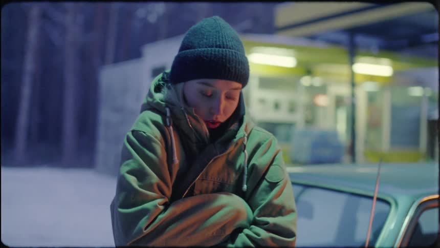 A young woman checks her smartphone while standing outside her vehicle in winter at a gas station
