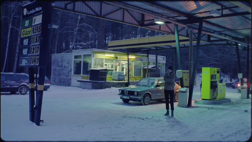 A woman walks around a car at the gas pump
