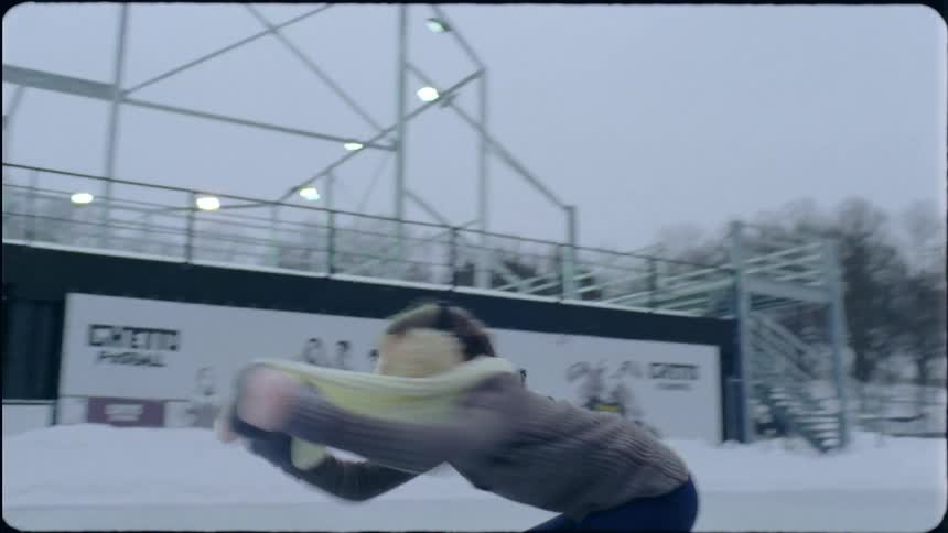 A woman twirls and figure skates on the ice of an outdoor rink on a cloudy day