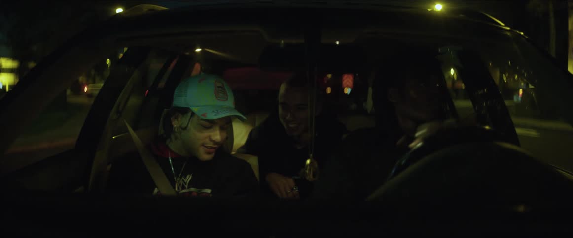 Three teenagers are traveling in an automobile and the driver is keeping his eyes on the road while the two passengers are talking