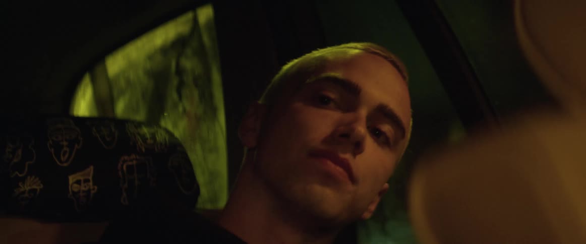 A teen in the backseat leans forward and talks to the driver while they drive at night