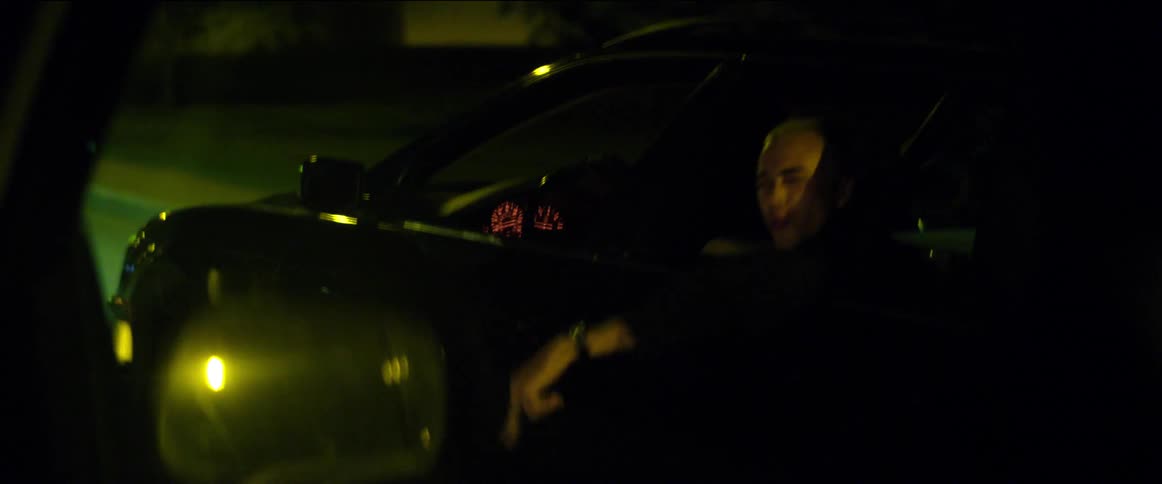 Teenagers are riding around in an automobile and one boy is hanging out of the window yelling and making aggressive hand motions to someone