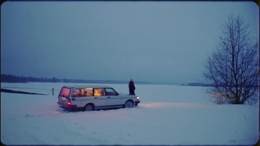 A person stands by their car near the snow filled field