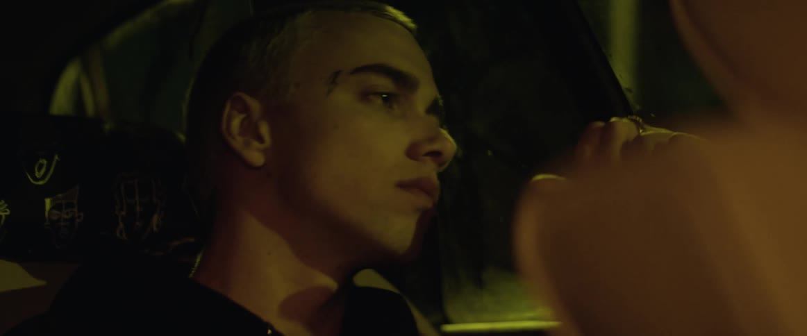 A teenage boy sits in the back seat of a car as it drives at night