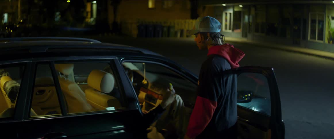 Two young men stay behind at the car talking and laughing as another walks away