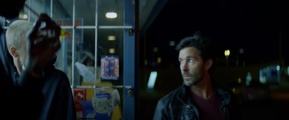 Two teenagers are going into a store as a man coming out the door turns around and looks at them and another man is standing outside the door smoking a cigarette