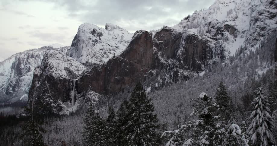 A mountain pass leads to trees below covered with snow