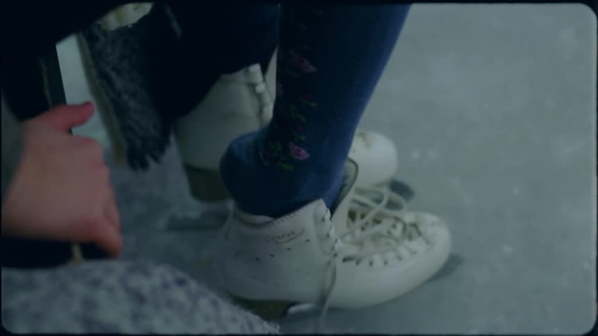 A woman sitting putting on her other ice skate at an outdoor rink