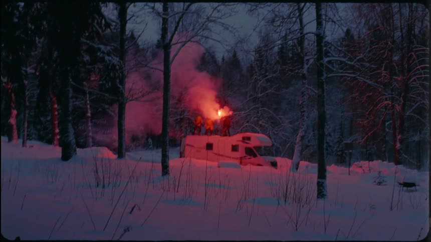 In winter people stand on top of camper in forest and move smoking flare around