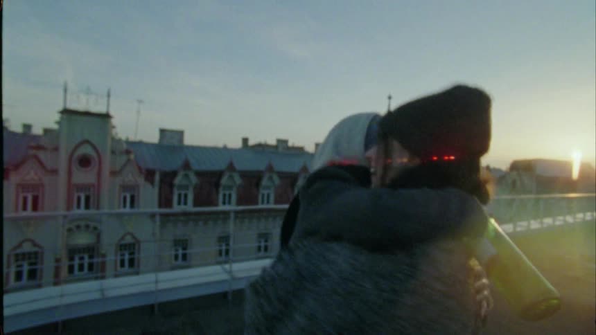 Two friends greet each other with a tight hug twirling on a rooftop overlooking european buildings
