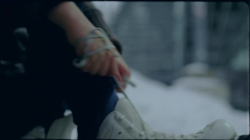 A woman ties the laces on her ice skates while sitting on a bench outside