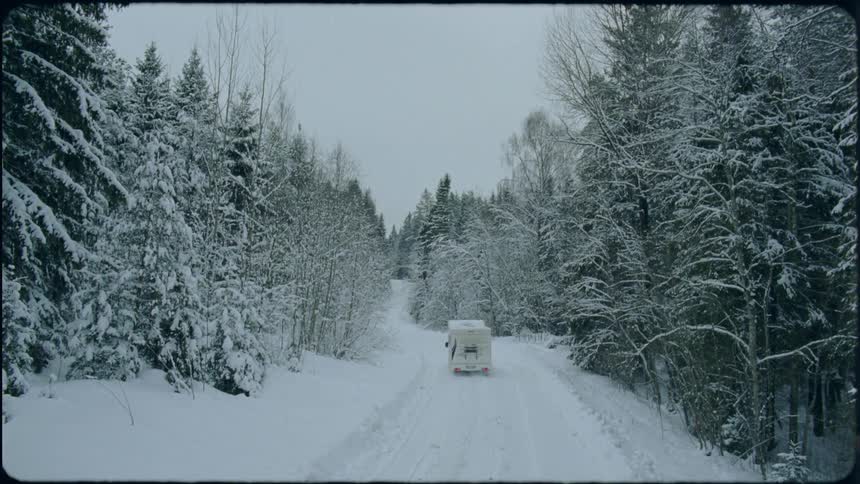 A motor home drives down a snowy road past a forest