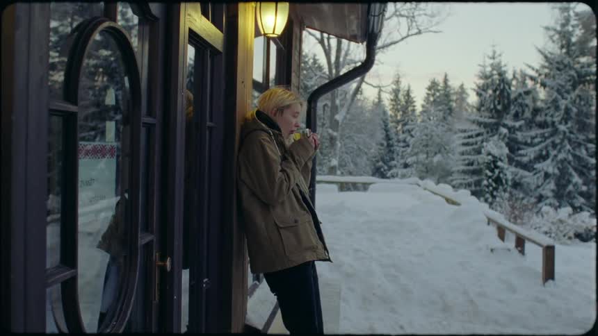 A teenage girl leans against a house and drinks wine