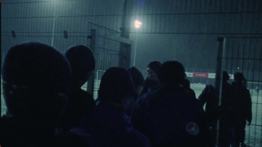 A group of people walk on to a snowy sports field at night