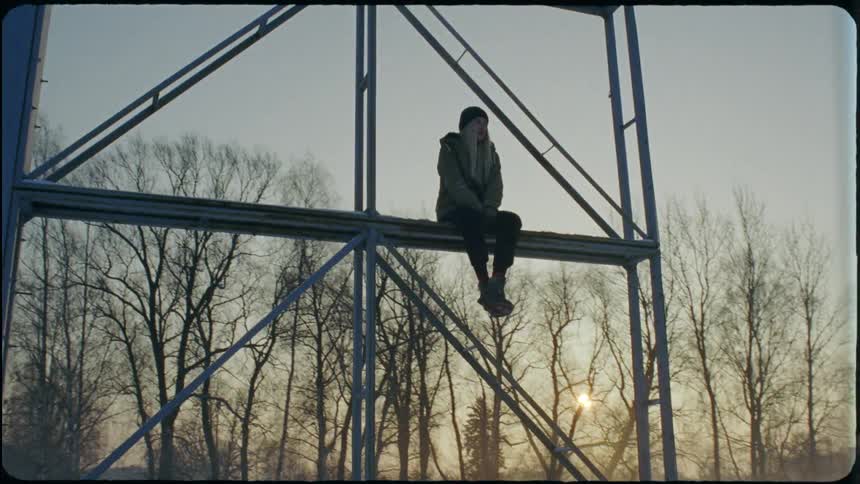 A young woman sits up on scaffolding in a snowy field
