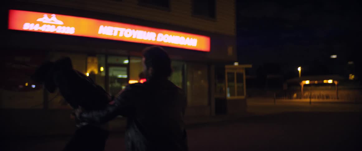 A man struggles as another man grabs him from behind and pulls him on a street in front of a store at night