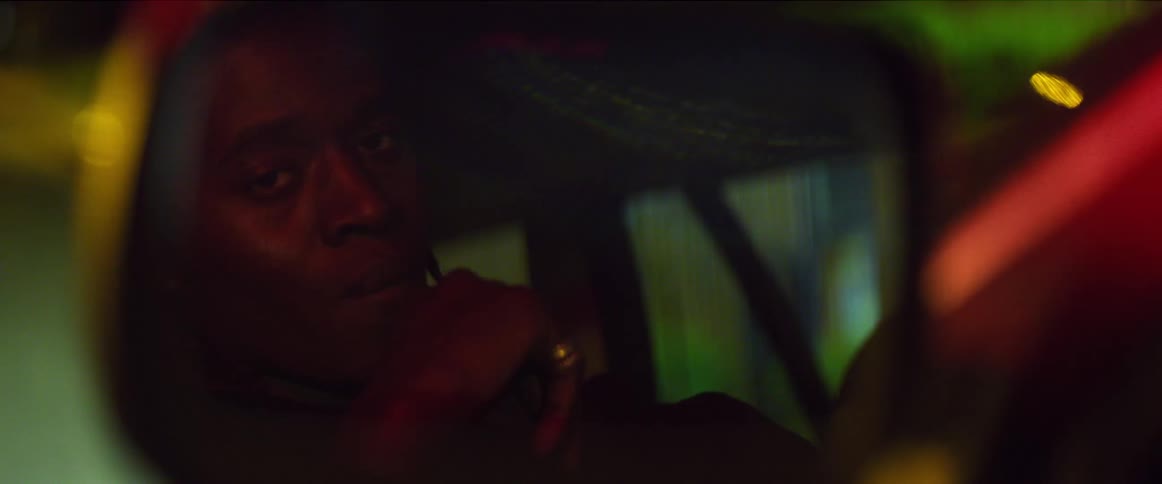 A young black man sits inside a car at night and looks around