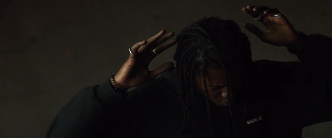 A young black man looks scared as he raises his hands above his head