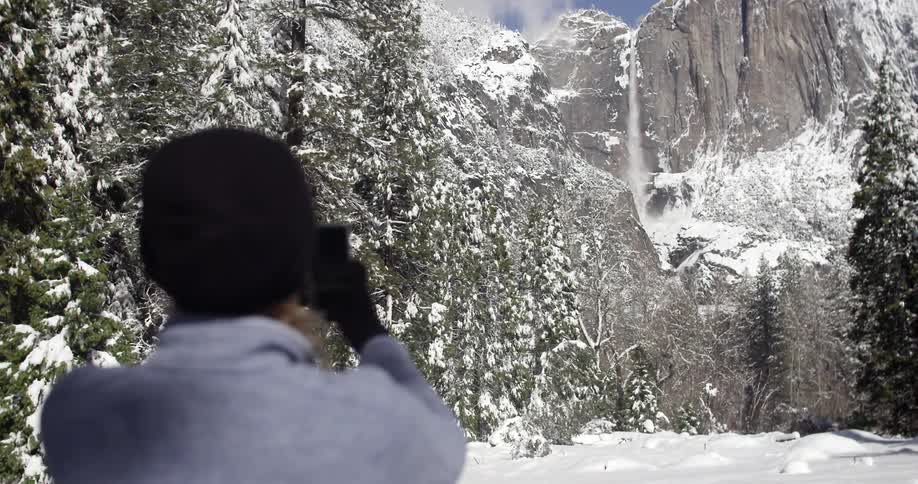 A man takes pictures of a snowy waterfall