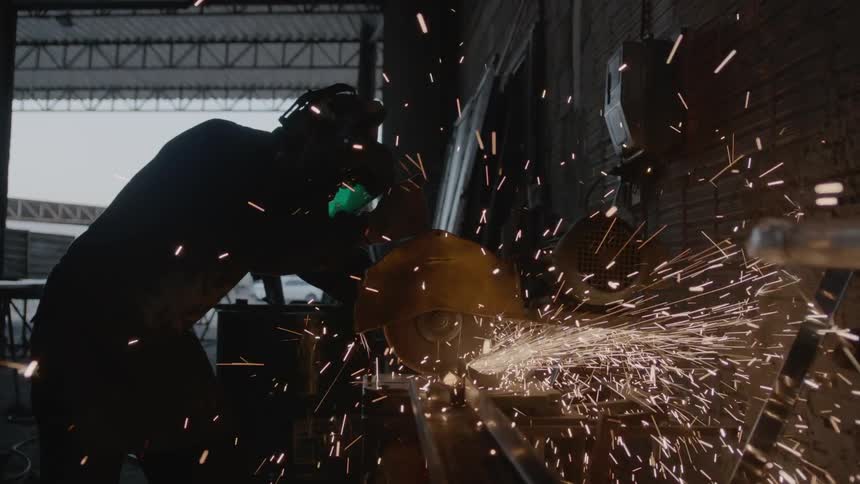 Sparks fly as a man turns on a saw in a hangar