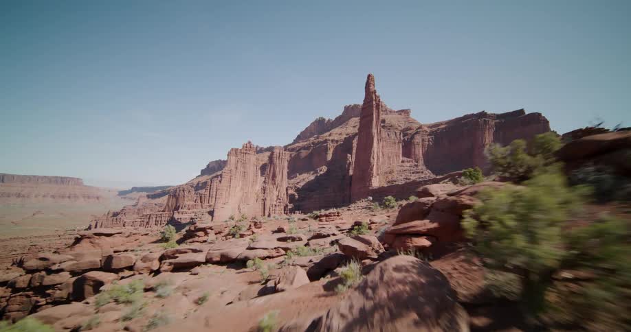 Moving through the desert badlands with plants scattered among buttes and rock formations with a mesa in the distance