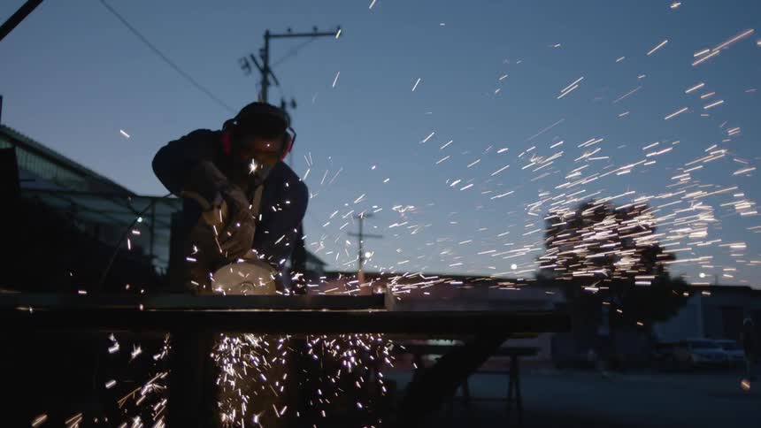 Sparks fly as a man is standing outside and using a circular saw to cut metal
