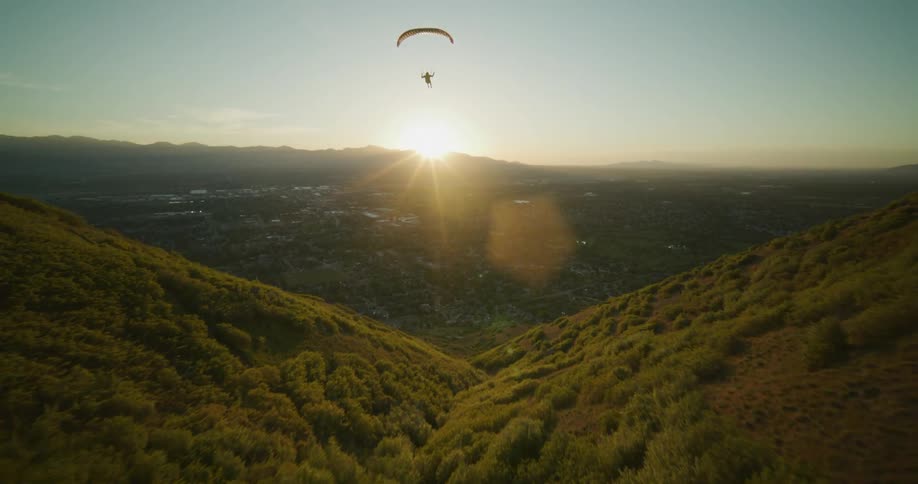 A paraglider flies over rolling hills