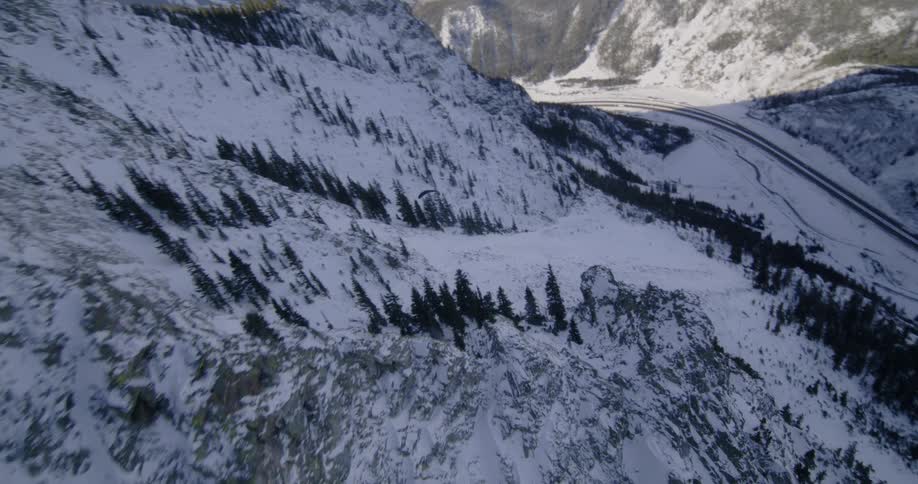 A paraglider is sailing through the air along a forested mountain slope and there is traffic on the highway below