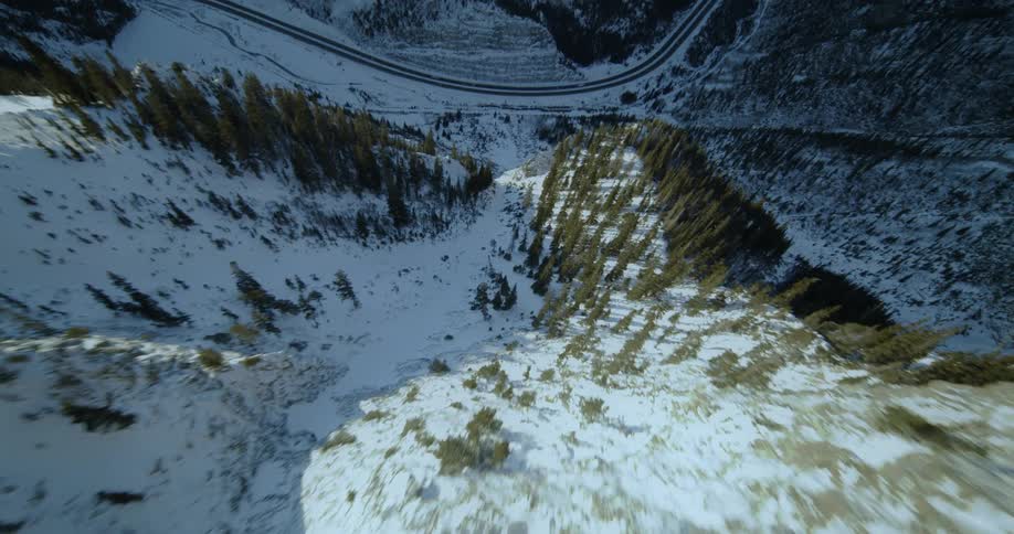 Heading down a steep mountain slope that is rocky and dusted with snow towards a road below