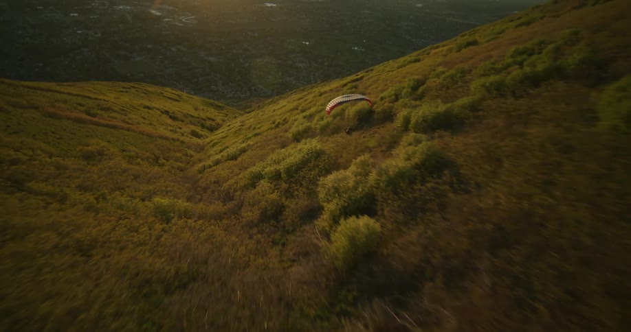A paraglider sails down a mountain slope turning and flipping in the air