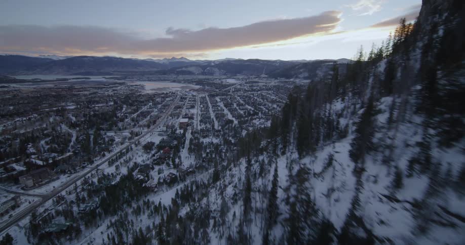 A dusting of snow covers a neighborhood below a forest along a hill