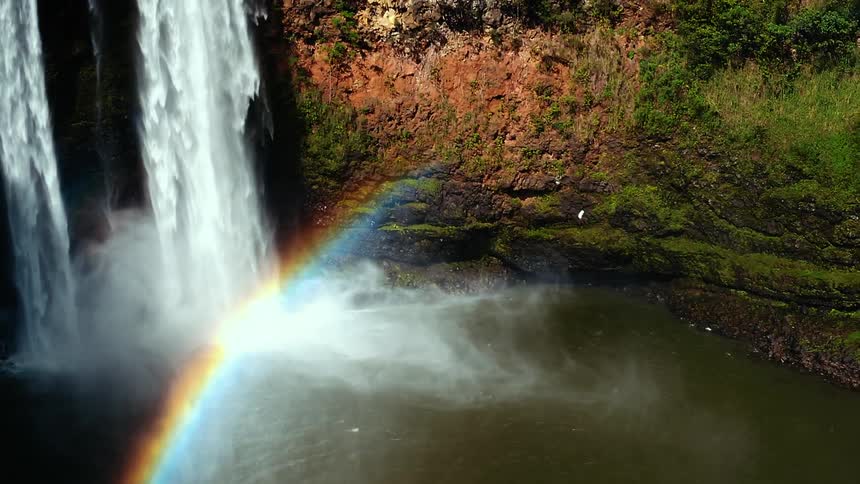 A rainbow forms near waterfalls and a lake