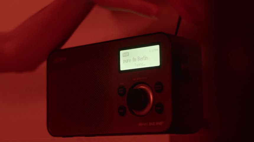 Person turns on radio sitting on shelf in room lit by red lighting
