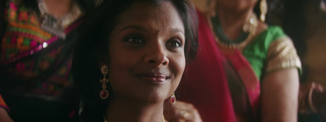 A woman smiles as two other women tend to her hair and jewelry