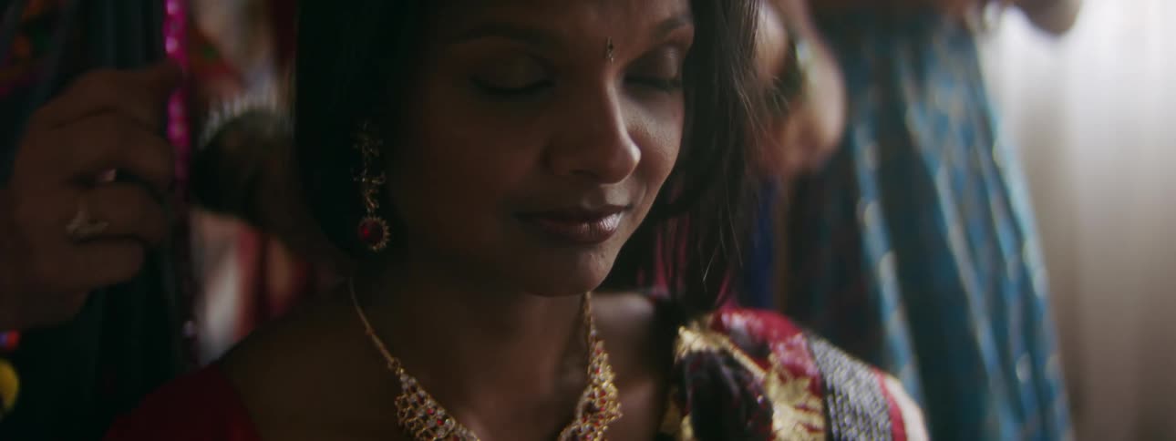 Women put jewelry on a young hindi teenage woman sitting on a chair at home