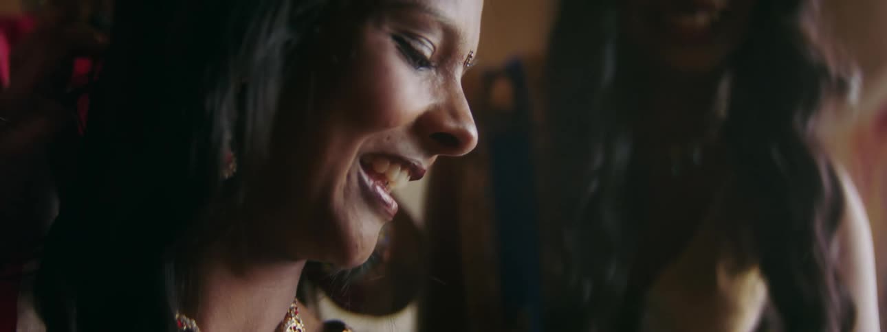 A woman smiles as a woman behind her fixes her hair and another woman is near her watching