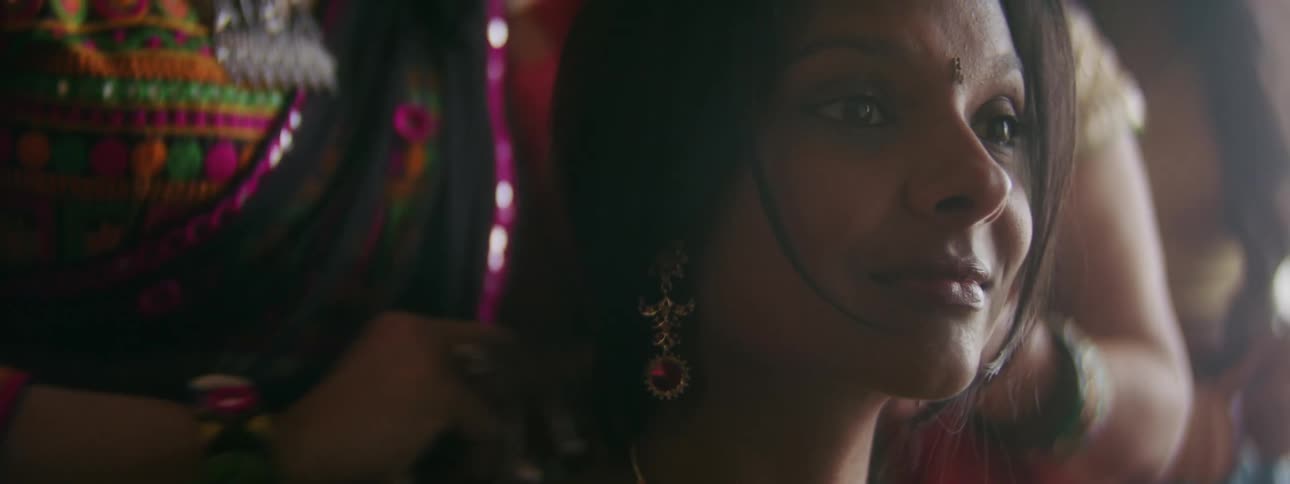A woman smiles as two women put a gold necklace on her