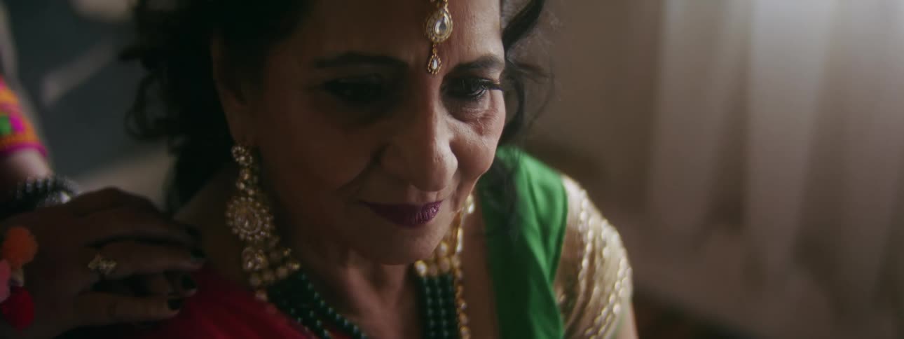 An indian woman is dressed up in colorful clothes and jewelry as she sits down and cries someone has their hand on her shoulder